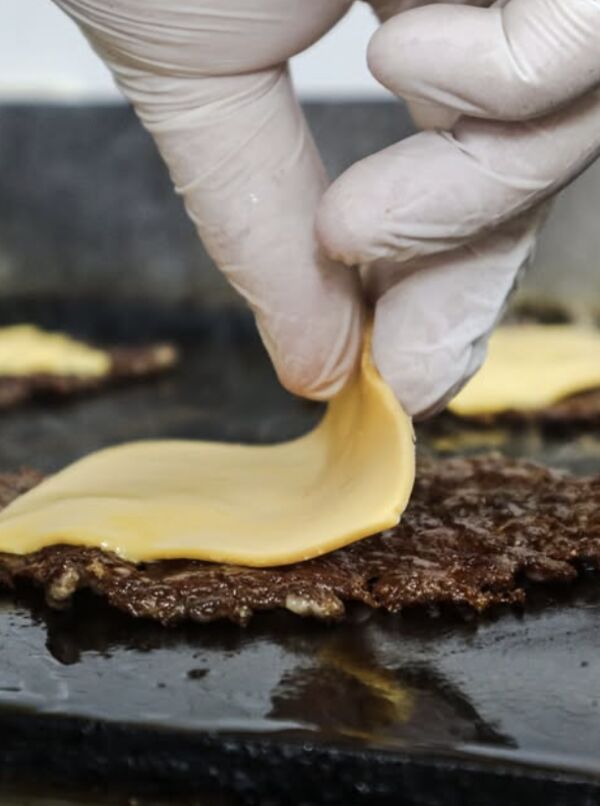 Tranche de cheddar posée sur un steak smashé, sur la plancha